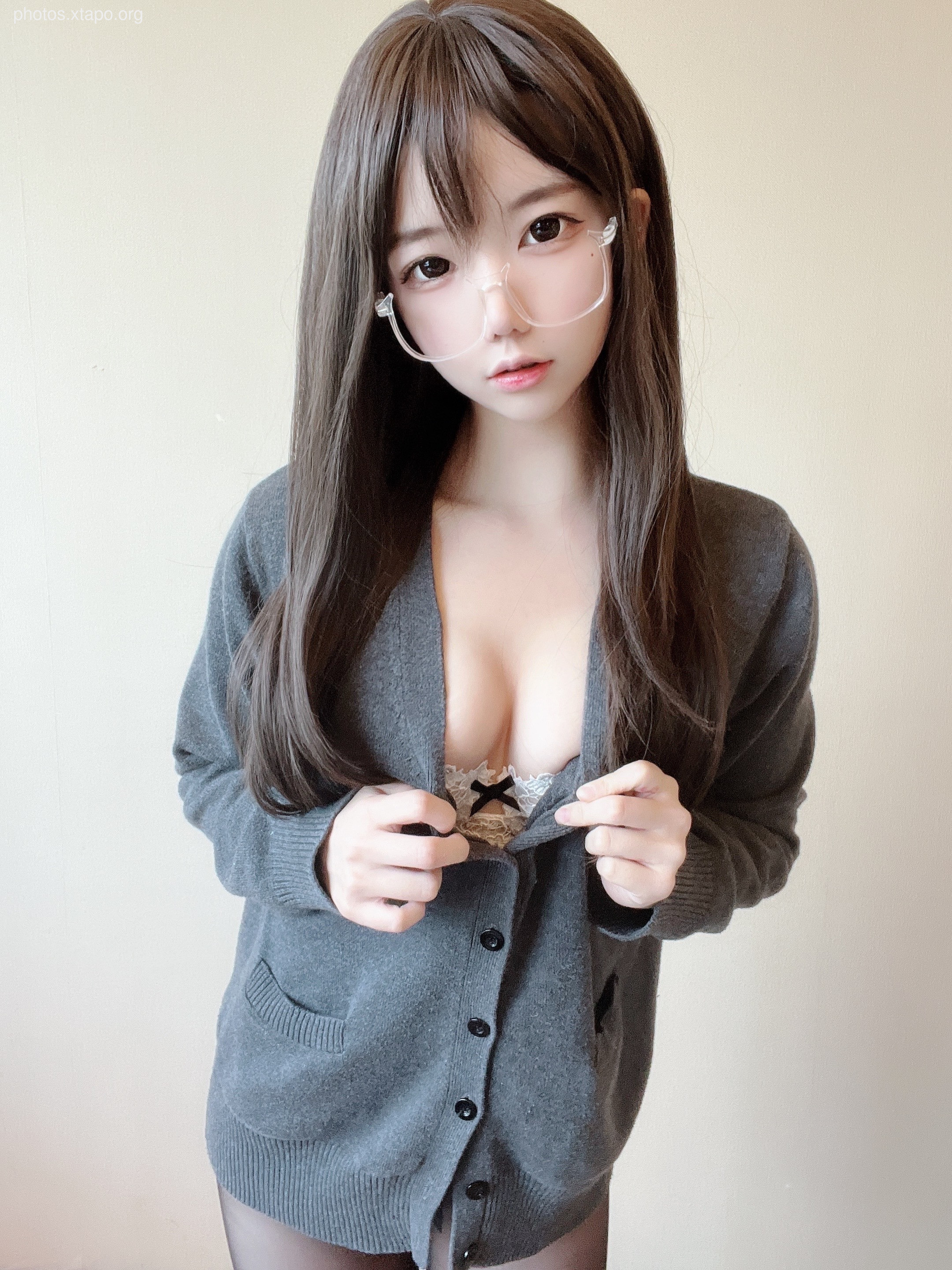 A young woman with long brown hair wearing glasses and a gray cardigan.